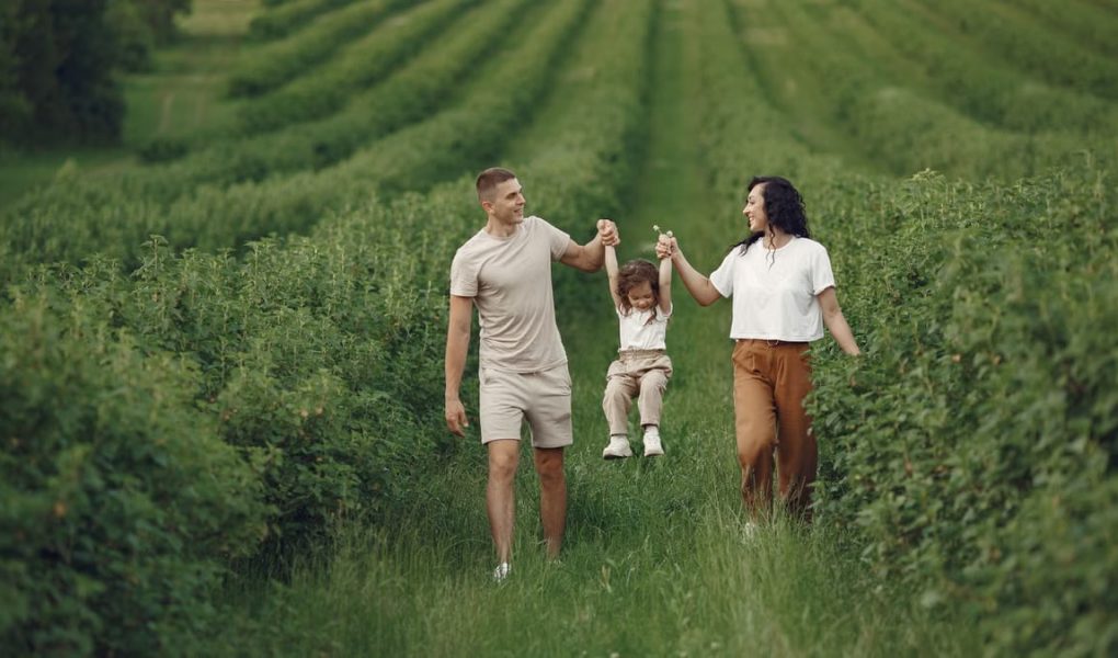 A happy family walking in a lush, green rural field together.